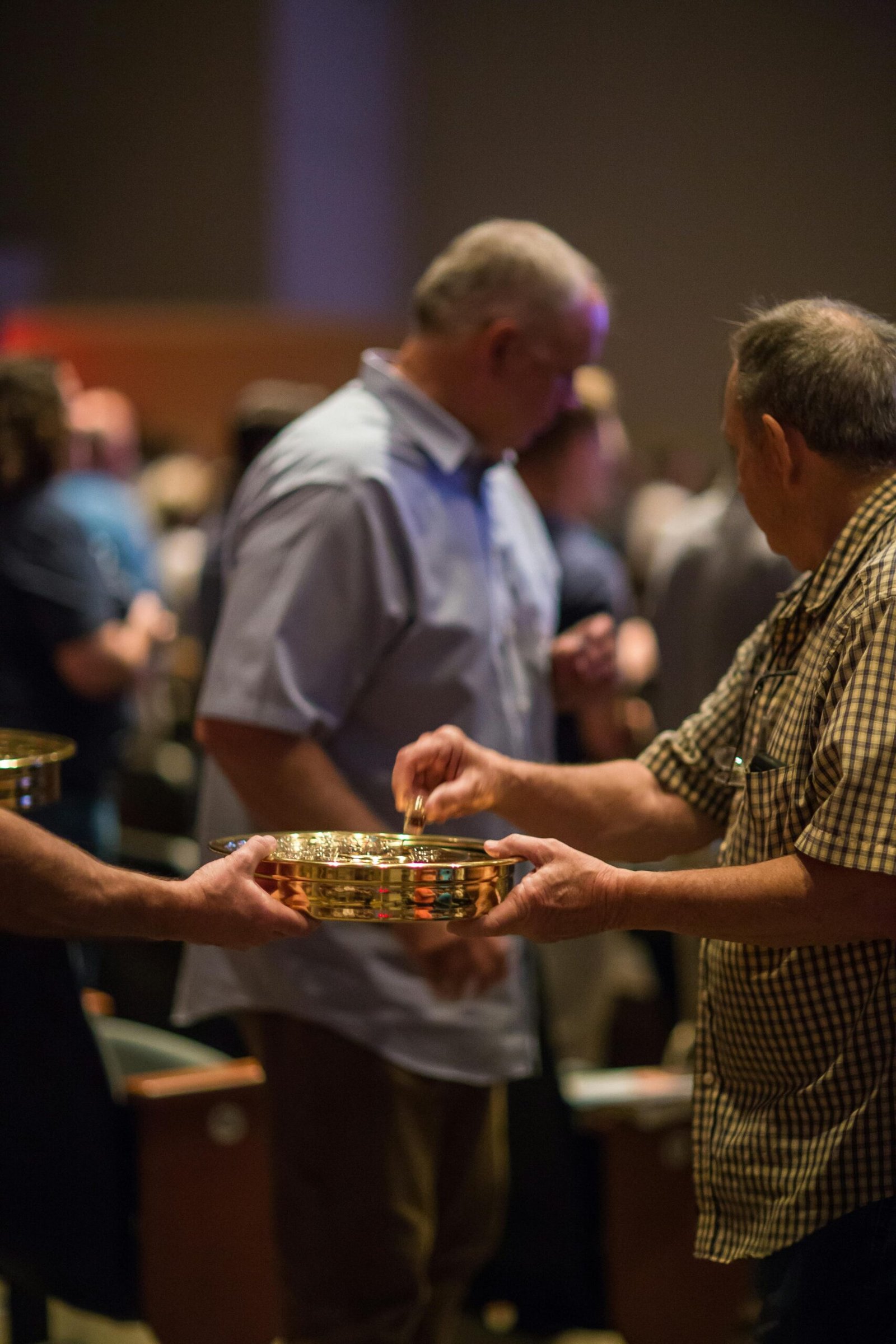 Men exchanging collection plates during a church service indoors.