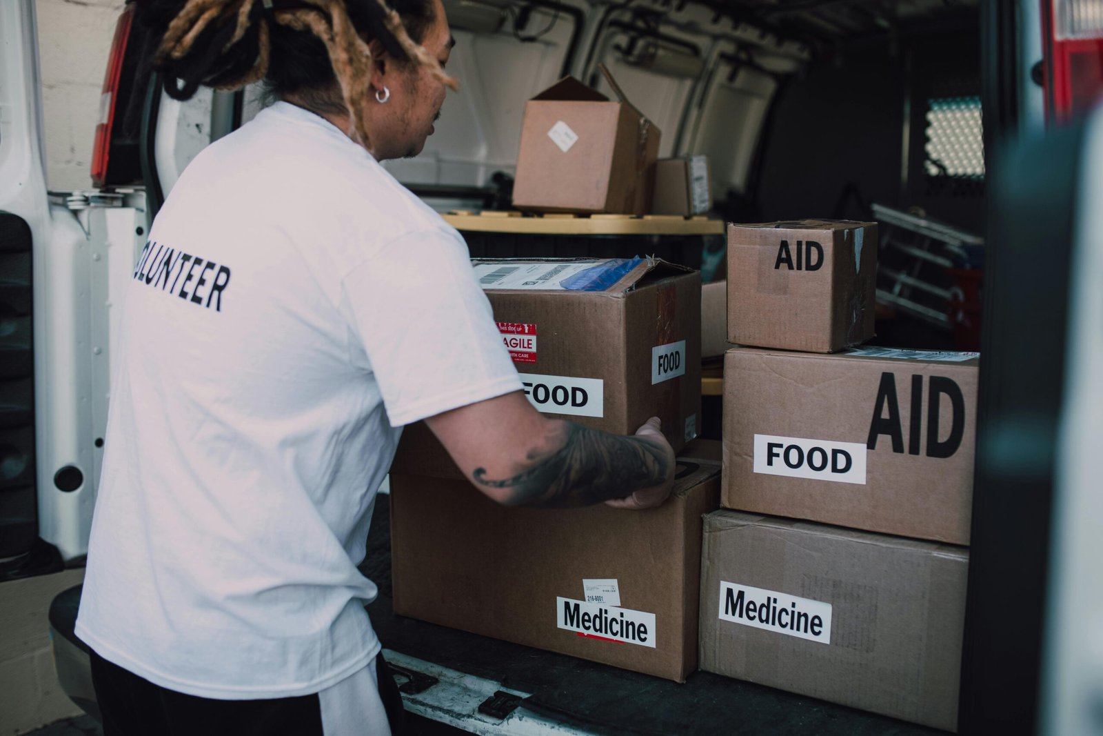 A volunteer organizes aid boxes containing food and medicine in a van for community service.