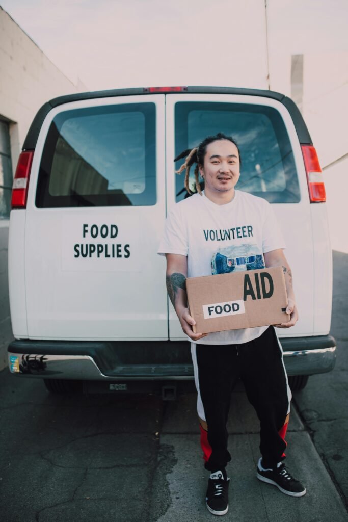 Volunteer holding food aid box in front of a van for community service donation.